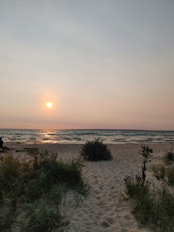 Sunrise over waters of Lake Michigan; beach and vegetation in foreground. 